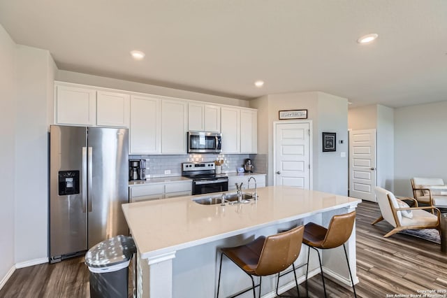 kitchen featuring dark wood-type flooring, a sink, stainless steel appliances, white cabinets, and decorative backsplash