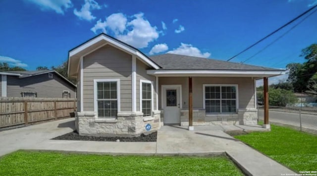 rear view of property with stone siding, a shingled roof, and fence