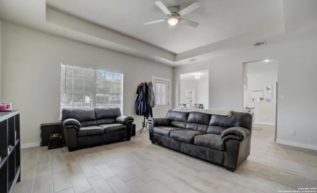 living room featuring a raised ceiling, baseboards, visible vents, and ceiling fan