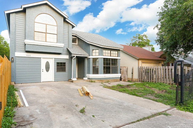 traditional home with a shingled roof, concrete driveway, and fence