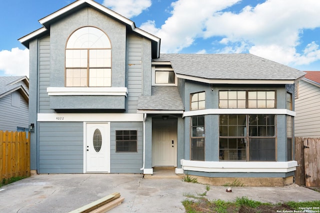 view of front facade featuring a patio, fence, driveway, stucco siding, and a shingled roof