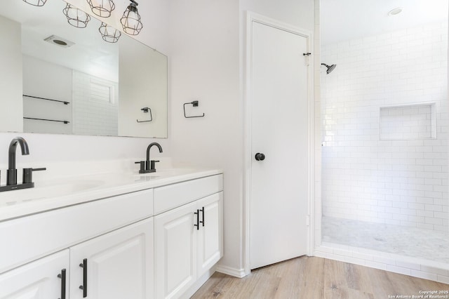 full bathroom featuring a tile shower, a sink, and wood finished floors