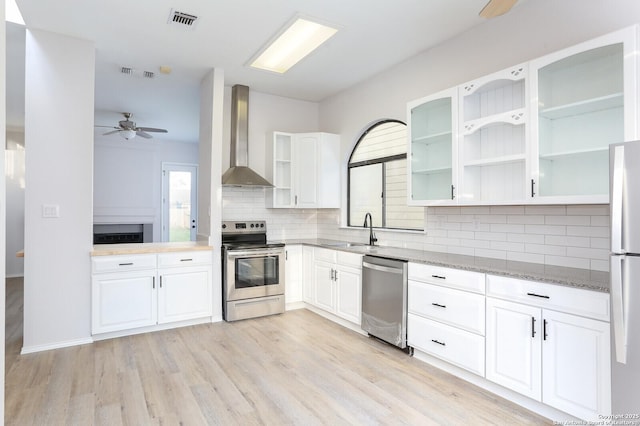 kitchen with visible vents, a sink, stainless steel appliances, wall chimney exhaust hood, and light stone countertops