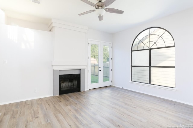 unfurnished living room featuring a ceiling fan, baseboards, light wood-style flooring, a fireplace, and french doors