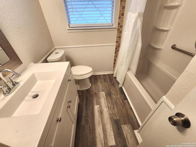 full bath featuring vanity, shower / bathtub combination with curtain, wood finished floors, toilet, and a textured wall