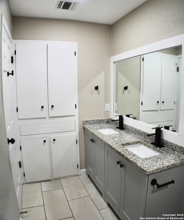 bathroom with double vanity, a textured wall, visible vents, and a sink