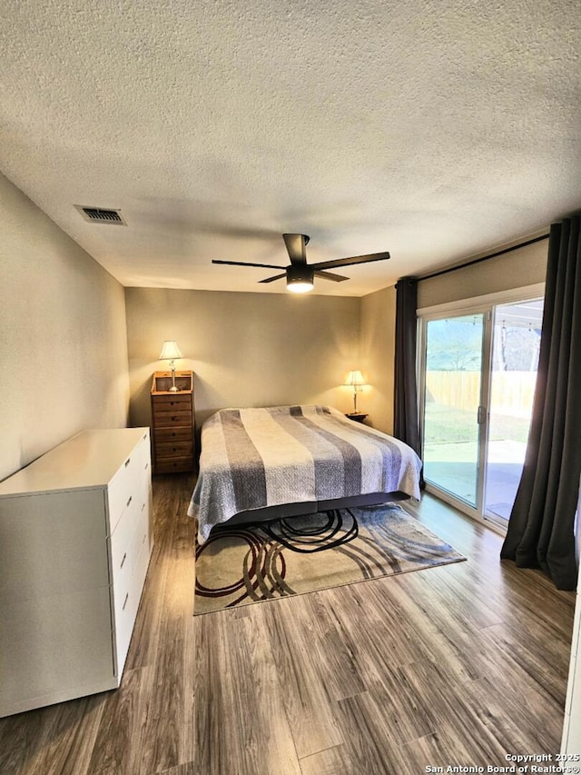 bedroom featuring visible vents, dark wood finished floors, ceiling fan, access to exterior, and a textured ceiling