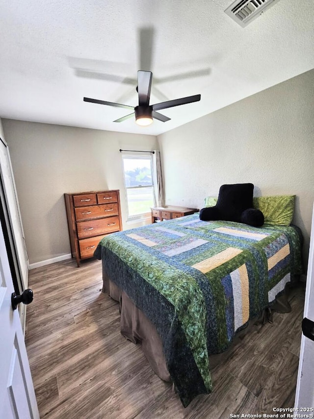 bedroom featuring visible vents, a textured ceiling, a ceiling fan, and wood finished floors