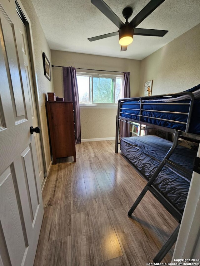 bedroom featuring a ceiling fan, a textured ceiling, wood finished floors, baseboards, and a textured wall