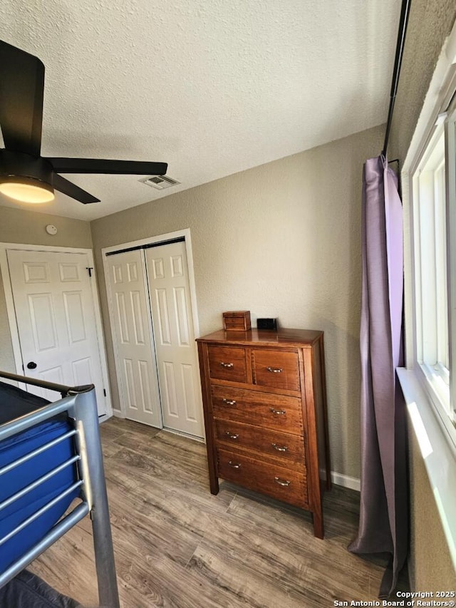 bedroom with wood finished floors, visible vents, ceiling fan, a closet, and a textured ceiling