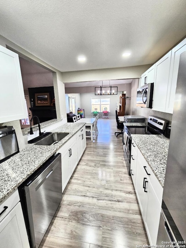 kitchen with light wood-type flooring, a sink, appliances with stainless steel finishes, white cabinets, and light stone countertops