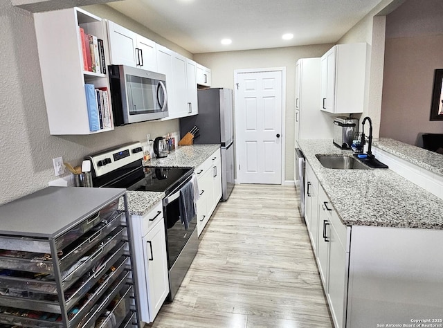 kitchen featuring light stone counters, appliances with stainless steel finishes, light wood-style floors, white cabinetry, and a sink