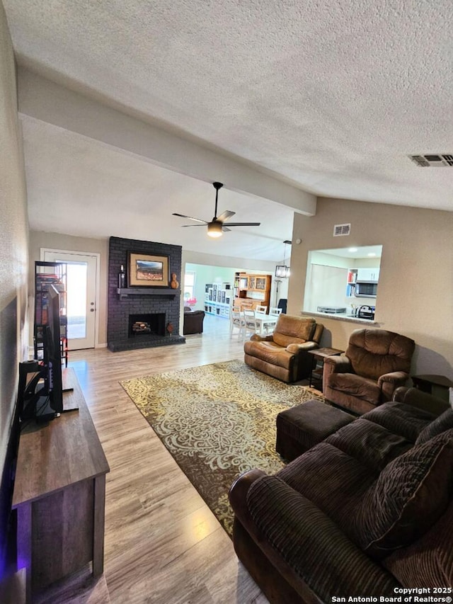 living area featuring wood finished floors, visible vents, vaulted ceiling, a textured ceiling, and a brick fireplace