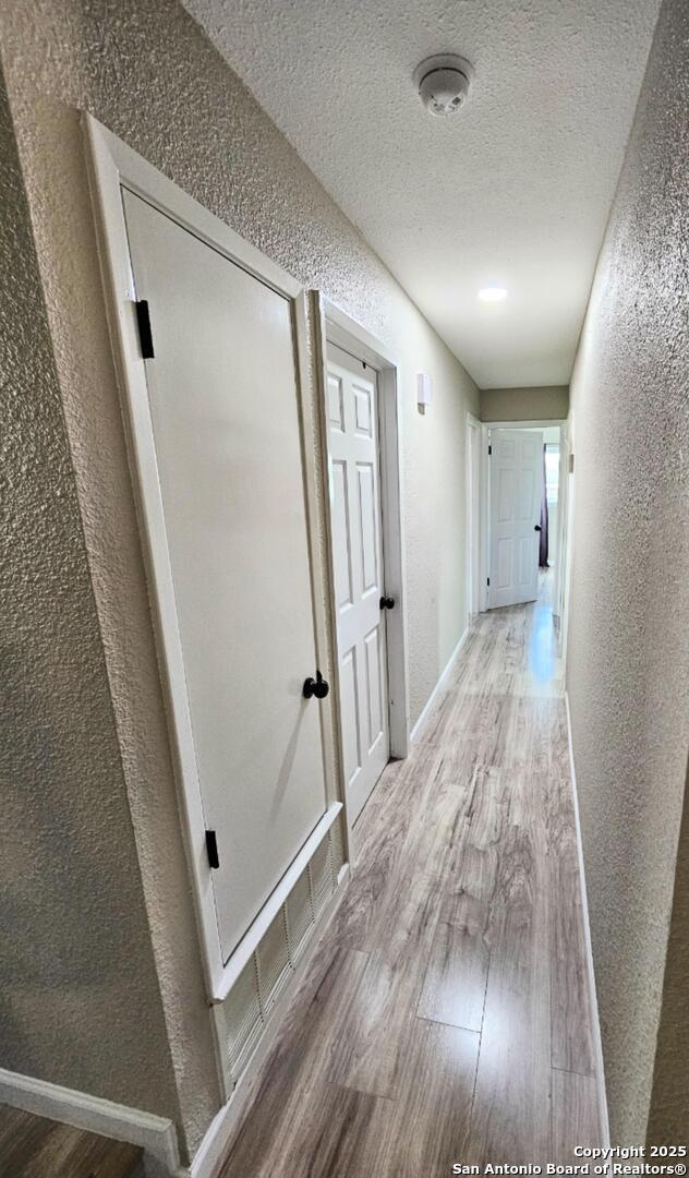 corridor with a textured ceiling, wood finished floors, baseboards, and a textured wall