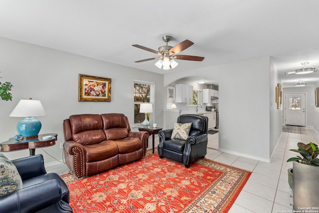 living room featuring light tile patterned floors, arched walkways, baseboards, and a ceiling fan