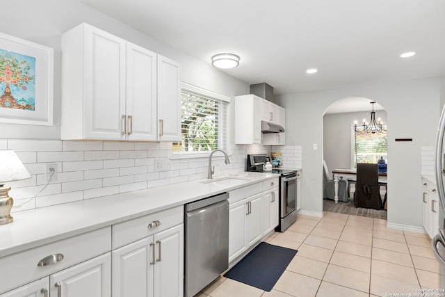 kitchen with a sink, under cabinet range hood, stainless steel appliances, arched walkways, and light tile patterned floors