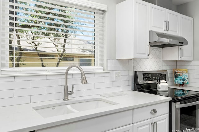 kitchen featuring stainless steel range with electric stovetop, under cabinet range hood, a sink, backsplash, and white cabinets