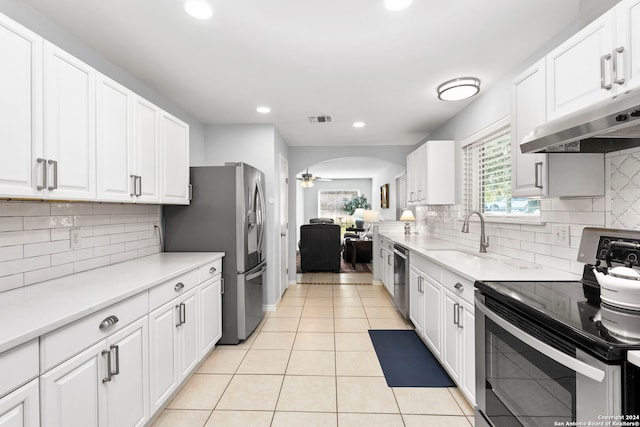 kitchen featuring under cabinet range hood, a sink, stainless steel appliances, arched walkways, and light tile patterned floors