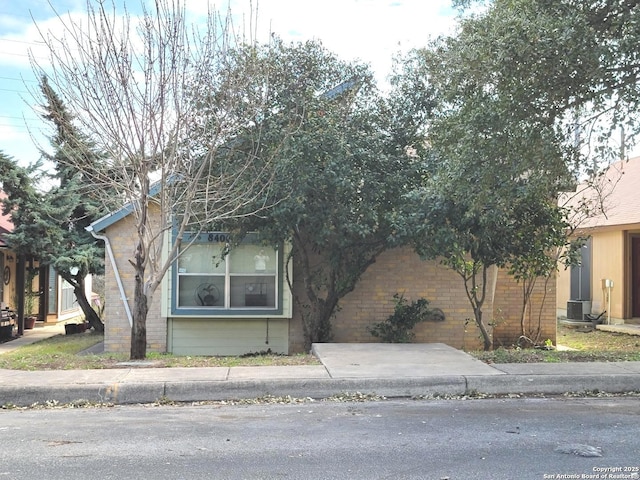 view of property hidden behind natural elements featuring brick siding and central AC