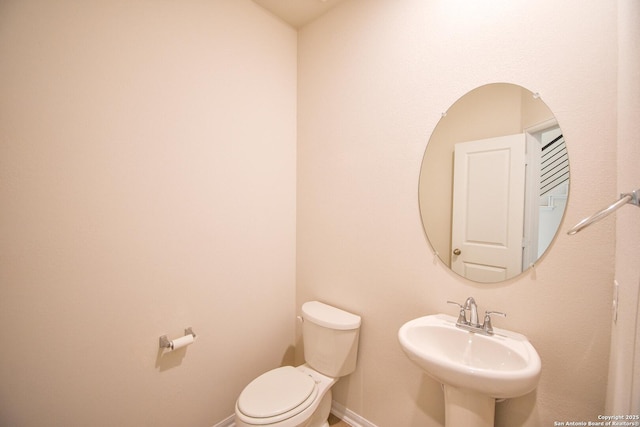 half bath with toilet, baseboards, and a sink