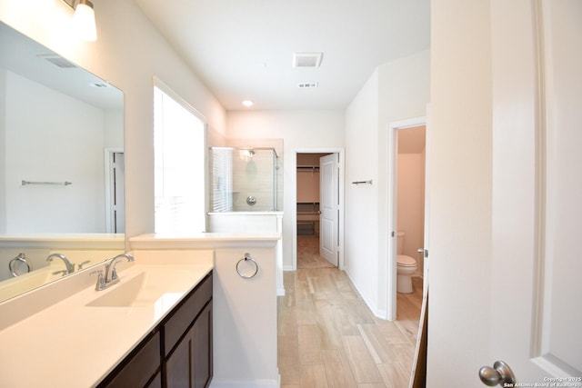 bathroom featuring vanity, wood finished floors, a stall shower, a spacious closet, and toilet