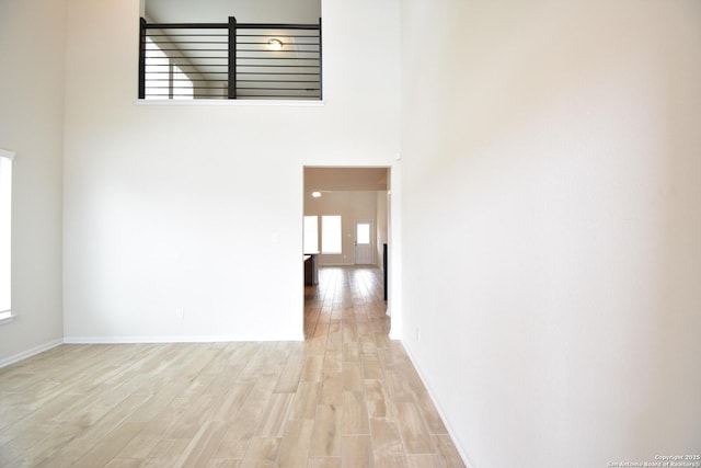 empty room featuring a high ceiling, baseboards, and light wood finished floors