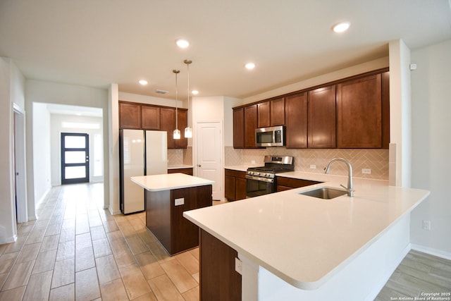 kitchen with wood finish floors, a sink, decorative backsplash, stainless steel appliances, and a center island