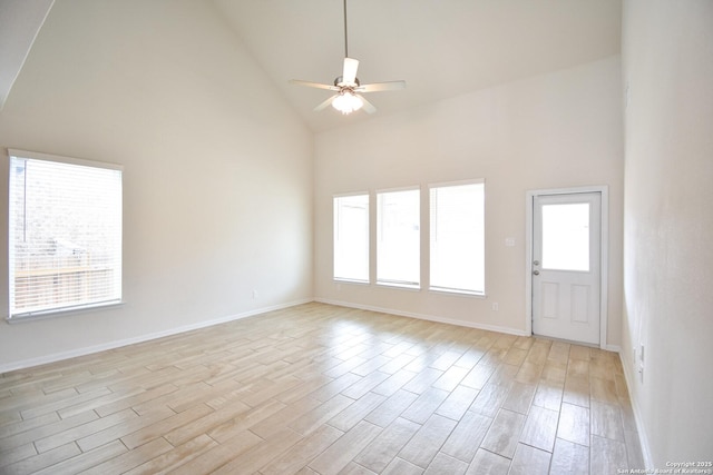 empty room with baseboards, high vaulted ceiling, ceiling fan, and light wood finished floors