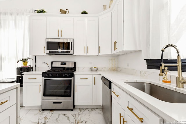 kitchen with light stone countertops, appliances with stainless steel finishes, white cabinets, marble finish floor, and a sink