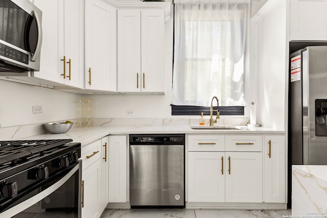 kitchen with light stone countertops, appliances with stainless steel finishes, marble finish floor, white cabinetry, and a sink