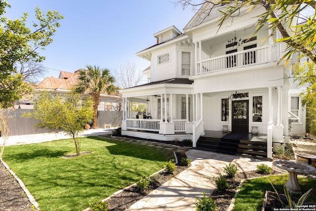 view of front of house featuring a front lawn, a balcony, fence, and covered porch