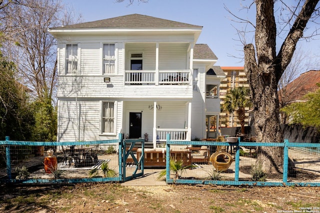 view of front of property with roof with shingles, a balcony, and fence