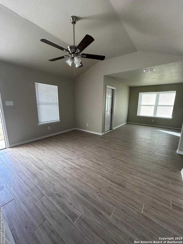 empty room with dark wood finished floors, a textured ceiling, baseboards, and vaulted ceiling