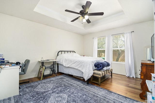 bedroom featuring a tray ceiling, wood finished floors, baseboards, and ornamental molding