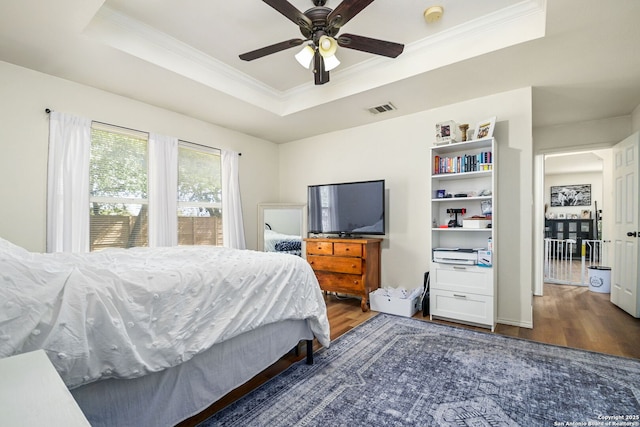 bedroom featuring visible vents, ornamental molding, wood finished floors, a raised ceiling, and a ceiling fan