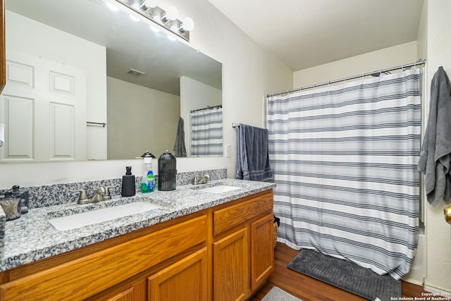 full bath with a sink, visible vents, wood finished floors, and double vanity