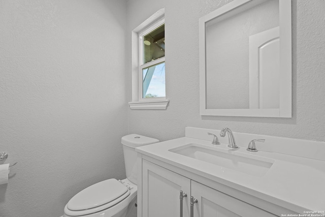 half bath with vanity, toilet, and a textured wall