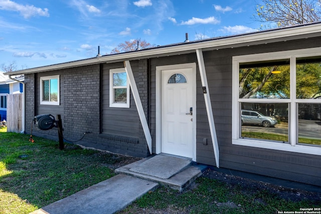 doorway to property with a lawn and brick siding