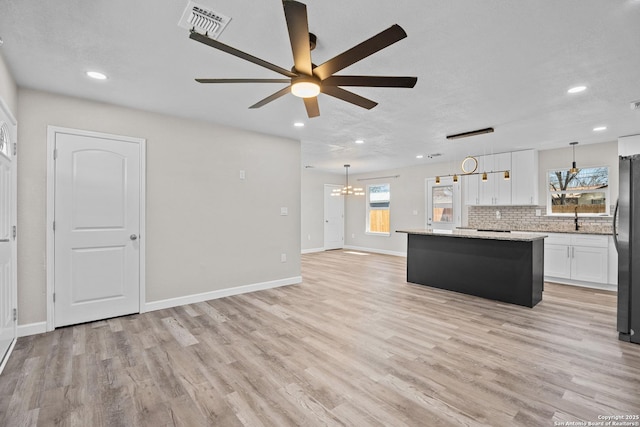 unfurnished living room featuring visible vents, ceiling fan with notable chandelier, light wood-type flooring, and baseboards