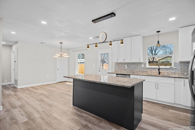 kitchen featuring decorative backsplash, a kitchen island, light wood-style floors, and a sink