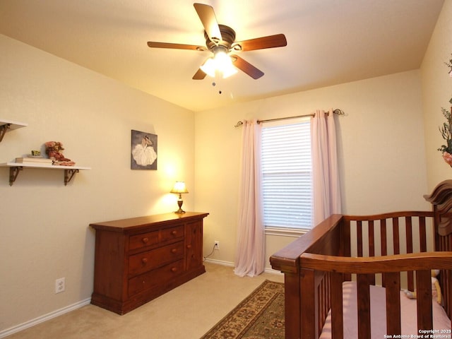 bedroom featuring baseboards, light carpet, a crib, and a ceiling fan