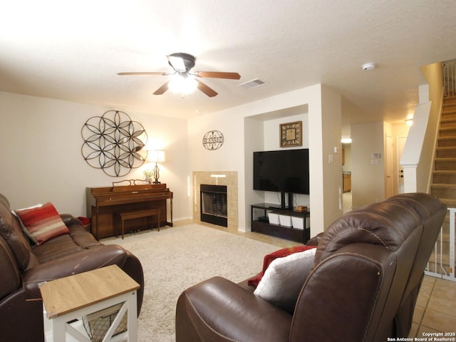 living room with visible vents, light carpet, stairway, ceiling fan, and a tile fireplace