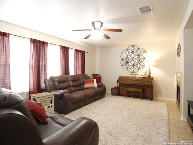 living area featuring light tile patterned floors, a ceiling fan, visible vents, baseboards, and a fireplace