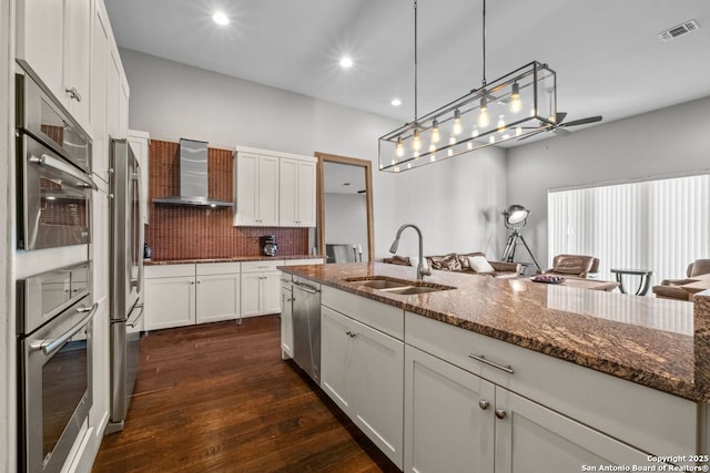 kitchen with visible vents, stainless steel appliances, a sink, white cabinets, and wall chimney range hood