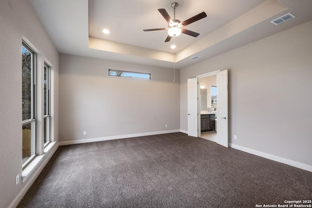 unfurnished bedroom featuring a tray ceiling, visible vents, baseboards, and carpet floors