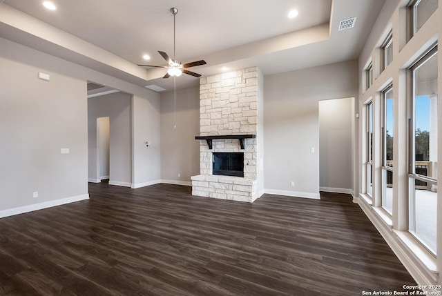 unfurnished living room featuring ceiling fan, baseboards, a tray ceiling, a fireplace, and dark wood-style flooring