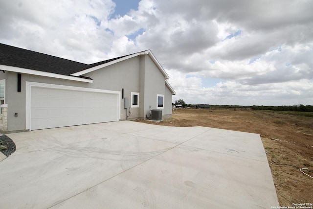 view of home's exterior featuring central air condition unit, stucco siding, concrete driveway, and a garage