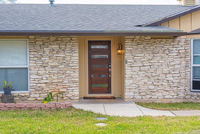 doorway to property with stone siding, board and batten siding, and roof with shingles