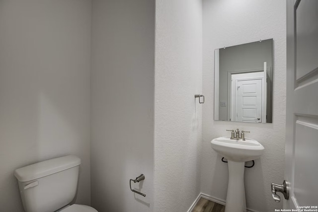 half bath with toilet, baseboards, and wood finished floors