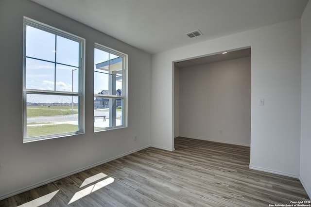 empty room featuring baseboards, wood finished floors, visible vents, and a healthy amount of sunlight